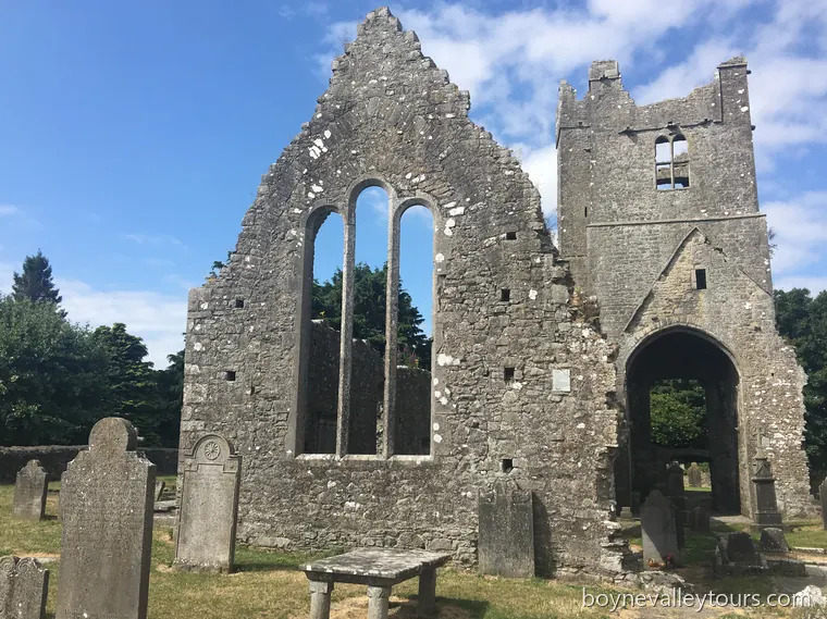 Roofless stone church and square tower of Duleek Abbey in a graveyard under a blue sky.
