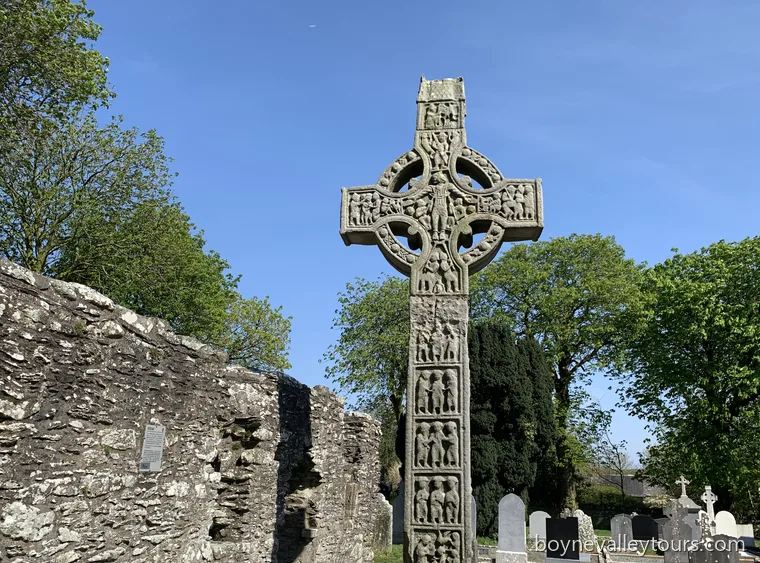Tall Cross at Monasterboice, a carved stone Celtic high cross beside ruined walls under a blue sky.